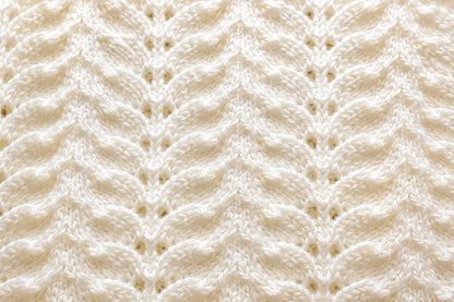 Elegant close up of antique white Wings baby blanket knitting pattern showing textured feather and lace stitch detail in soft ivory yarn