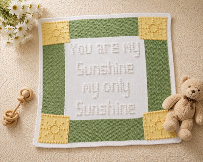 You Are My Sunshine baby blanket knitting pattern displayed on a cream nursery carpet with white flowers, a wooden rattle and a teddy bear