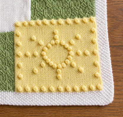 Close-up of the sunshine corner motif on the You Are My Sunshine baby blanket knitting pattern showing bobble stitch detail, textured green panels and white border