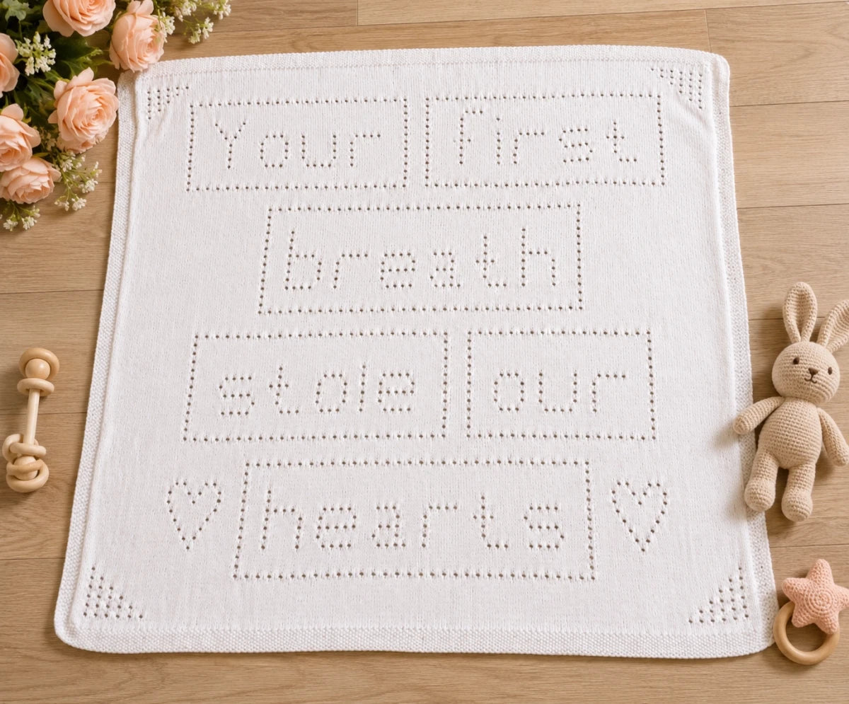 Your First Breath Stole Our Hearts baby blanket knitting pattern displayed on a wooden nursery floor with baby toys and soft peach flowers