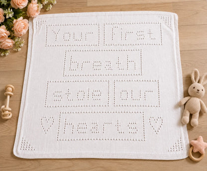 Your First Breath Stole Our Hearts baby blanket knitting pattern displayed on a wooden nursery floor with baby toys and soft peach flowers